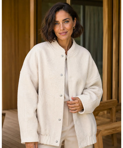 Woman layering oversized bouclé bomber jacket over a dress in nude